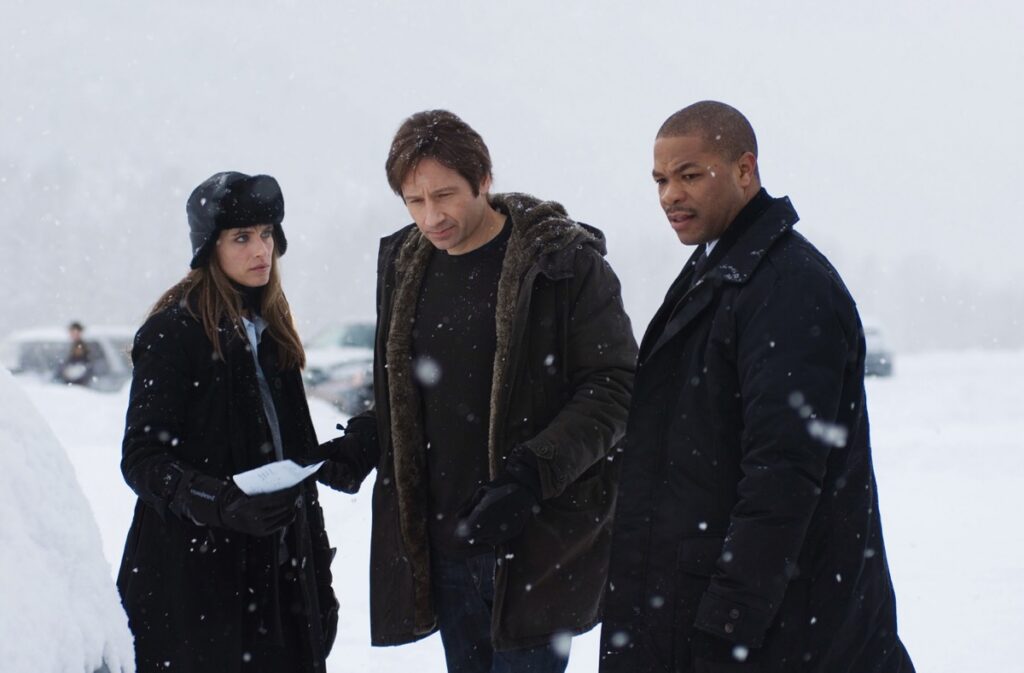 Two FBI agents flanking Fox Mulder in snowy terrain discussing a gruesome find
