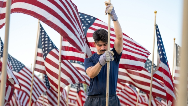 A college student installs a U.S. flag in the middle of a field of them