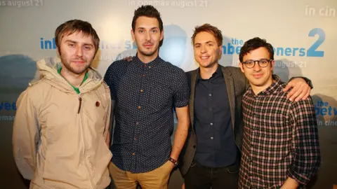 Getty Images James Buckley, Blake Harrison, Joe Thomas and Simon Bird pose at a premier of The Inbetweeners 2 in front of a billboard of the film. James wears a grey waterproof, Blake blue and white patterned top, Joe wears a grey blazer over a navy shirt and Simon wears checked patterned shirt.