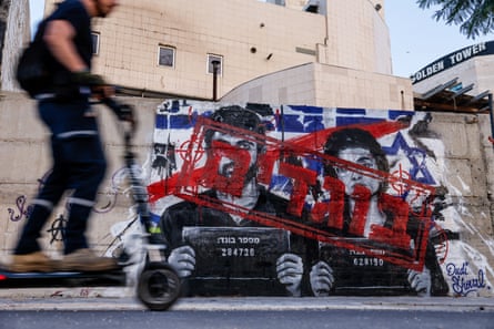 A blurred person in black on a scooter in foreground, with black, white, and red graffiti on a wall beyond.