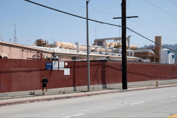 A person runs down a sidewalk past a ride fence with a facilities behind it.