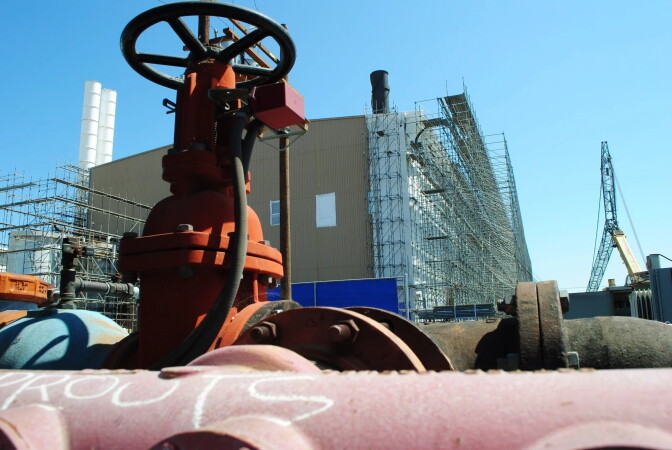 A close up of large water pipes outside with a large facilities in the background.