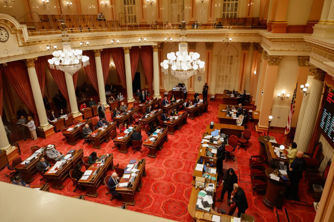 A high angle view looking down from a balcony to a senate floor where people are sitting at desks.