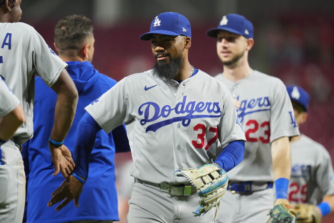 A dark-skinned man wearing a Los Angeles Dodgers baseball uniform gives a high five to a teammate on the field. More players can be seen exchanging high fives in the foreground and background.