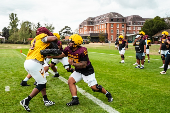 ASU football players practicing on a field in front of a red brick London resort building