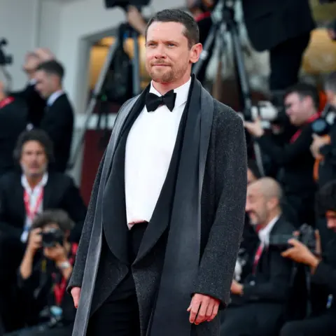 EPA Jack O'Connell looks towards camera while posing on the red carpet wearing a black tie outfit in Italy in September.