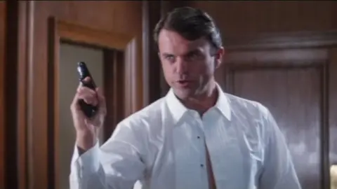 United Artists/EON/MGM Sam Neill in a white shirt and holding a gun as part of his audition for Bond