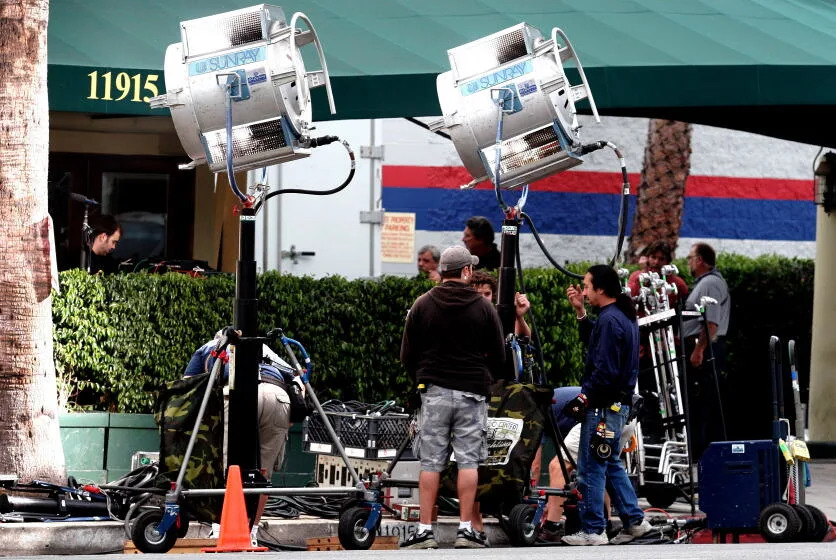 A production crew sets up lights on the side of a street.