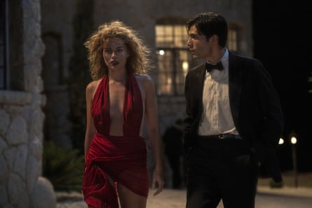 A woman in a red dress and a man in a tuxedo walk together at night
