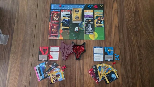 A tabletop game setup featuring game cards, character tokens, and a game board with various elements arranged on a wooden surface.